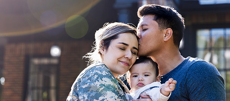 woman in military uniform holding baby next to man